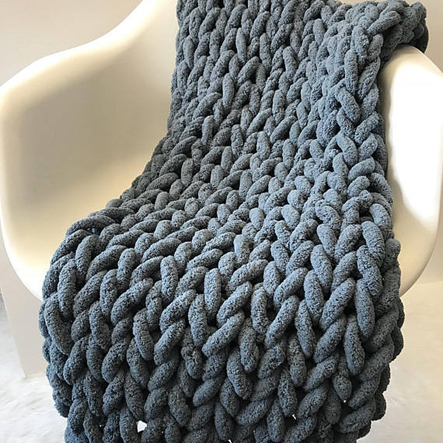 The Anchor chunky knit blanket in dark grey, draped over a white chair