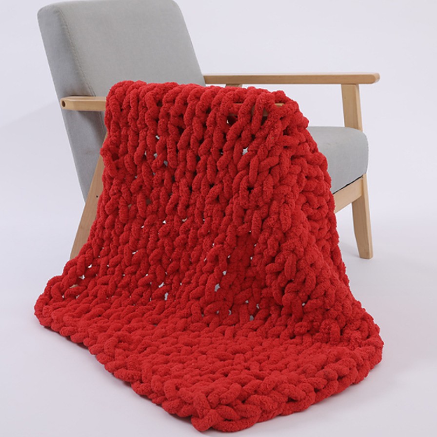 The Anchor chunky knit blanket in red, folded over the back of a grey armchair