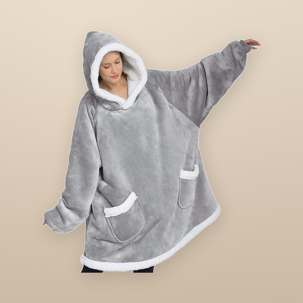 A woman wearing the Burrow oversized hoodie blanket in grey, arms stretched wide to show how big it is